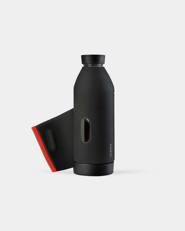 Reusable glass bottle with a soft touch and a patented strap making it hands-free. Double-opening for easy clean in black/coral.