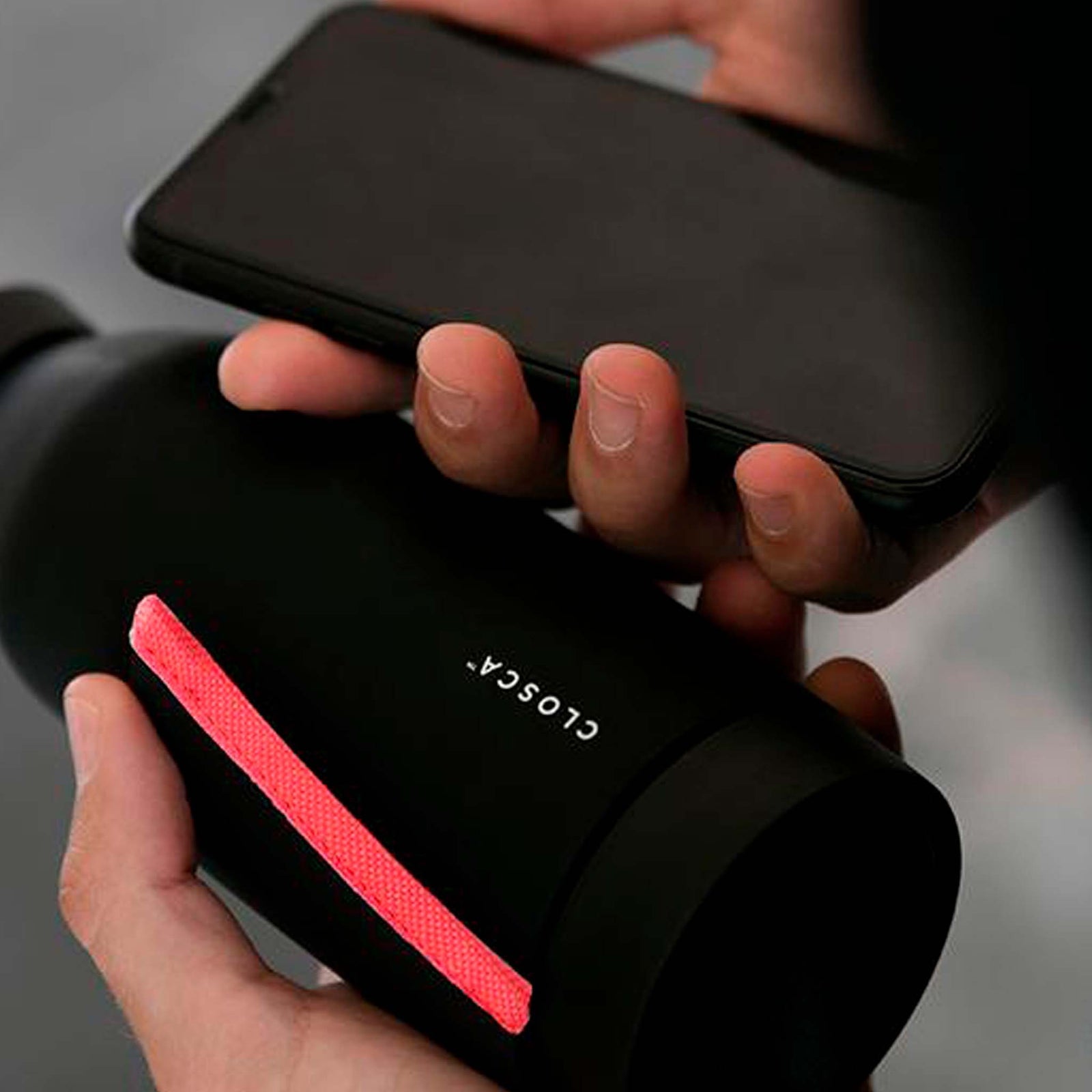 Reusable glass bottle with a soft touch and a patented strap making it hands-free. Double-opening for easy clean in black/coral.